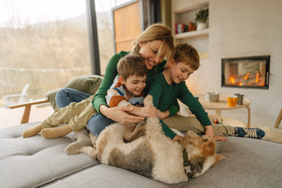 mother and three children cuddling the family dog on the sofa near a lit fireplace