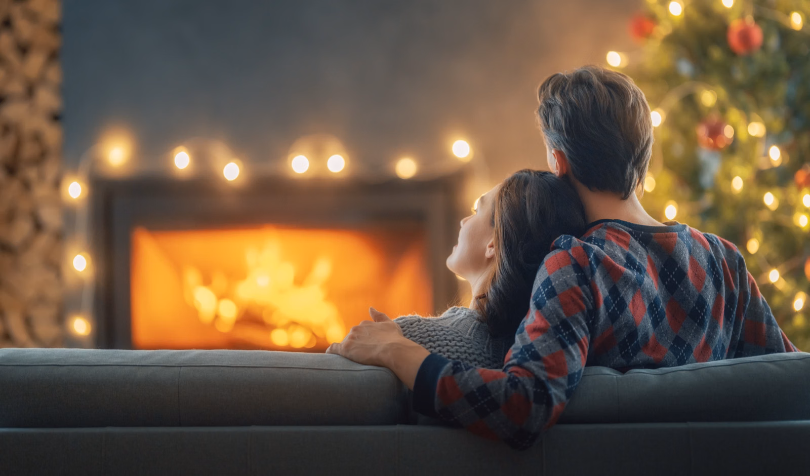Couple relaxing on the sofa in front of a glowing fireplace with holiday lights