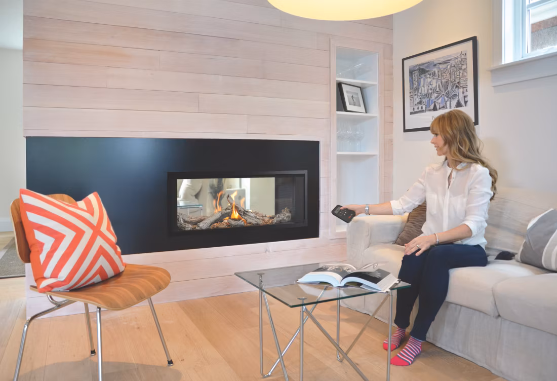 woman on sofa using remote with linear fireplace