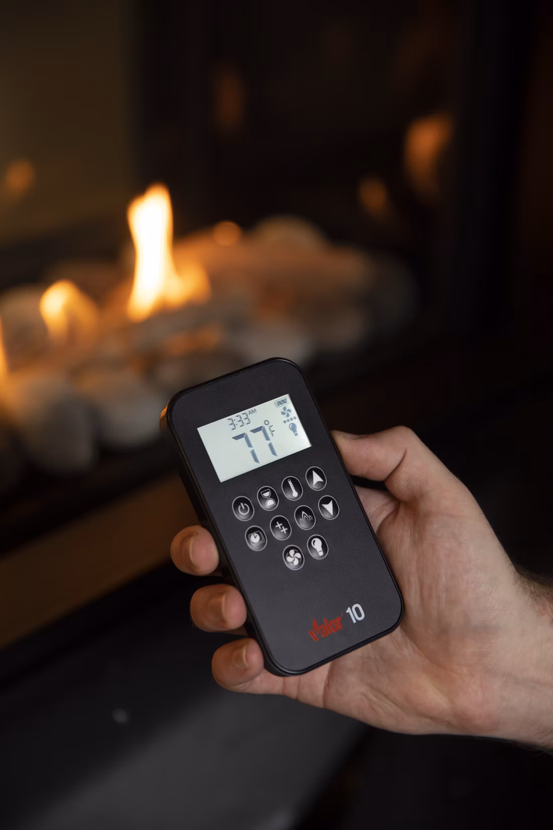 hand holding thermostat remote before glowing flames