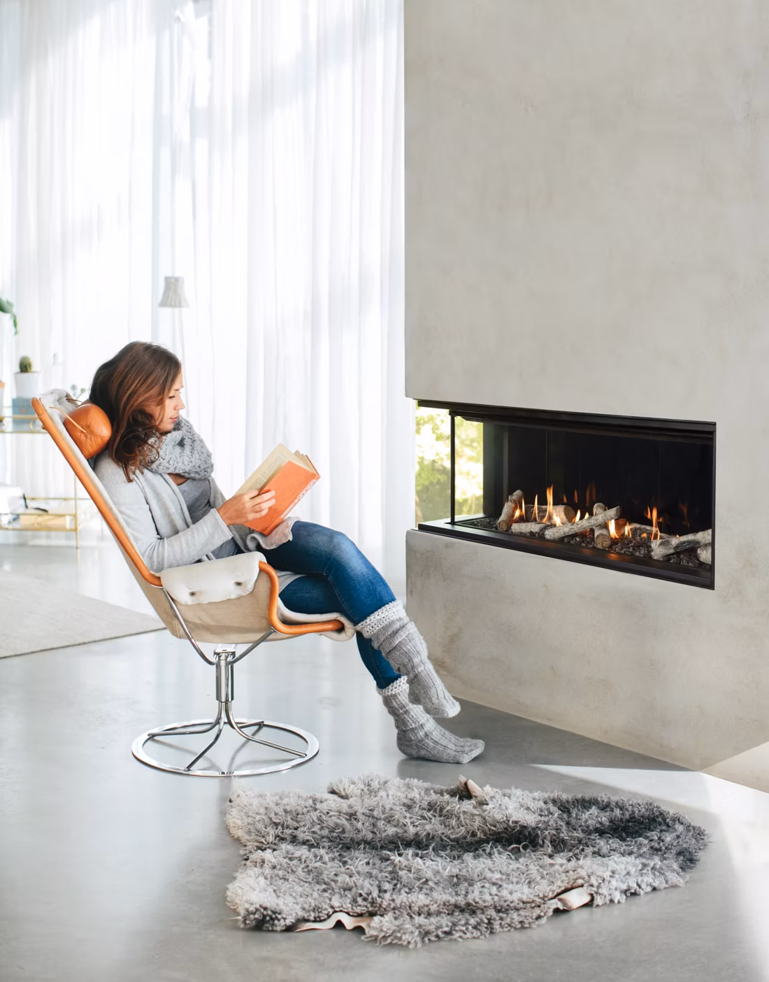 woman reading in chair by three-sided linear fireplace