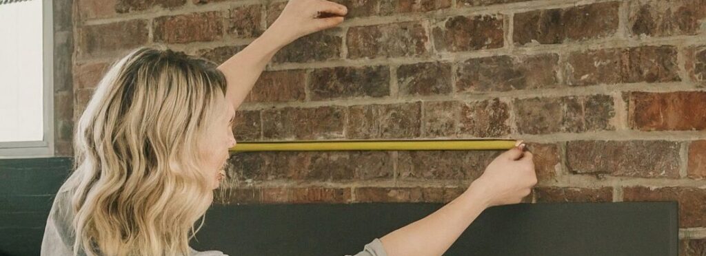 ![Person measuring an open brick fireplace with a tape measure for proper dimensions